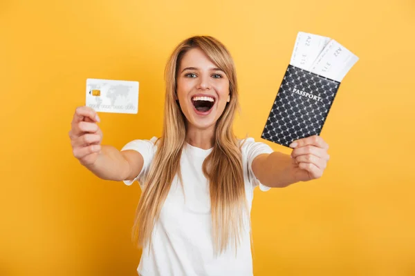 Positive junge blonde Frau springt isoliert über die gelbe Wand Hintergrund gekleidet in weißen lässigen T-Shirt mit Pass mit Tickets und Kreditkarte. — Stockfoto