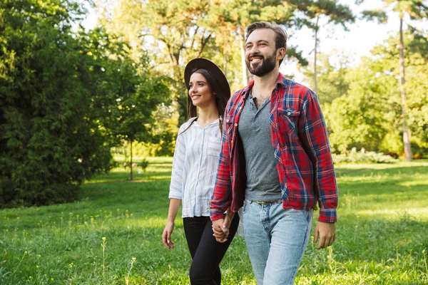 Kép a fiatal pár férfi és nő mosolyogva séta közben együtt zöld Park — Stock Fotó