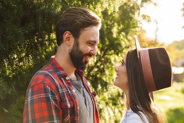 Image of brunette couple man and woman smiling while looking at each other in green park — Stock Photo, Image