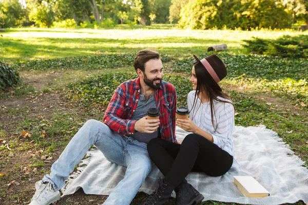 Bild eines glücklichen Paares, das im grünen Park Kaffee zum Mitnehmen trinkt — Stockfoto