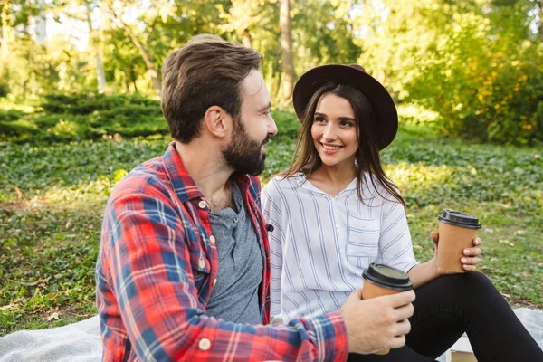 Imagen de pareja complacido hombre y womandrinking café para llevar mientras descansa en el parque verde —  Fotos de Stock