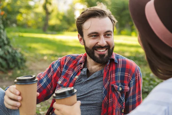 Imagen de una linda pareja de hombres y mujeres tomando café para llevar mientras descansan en el parque verde —  Fotos de Stock