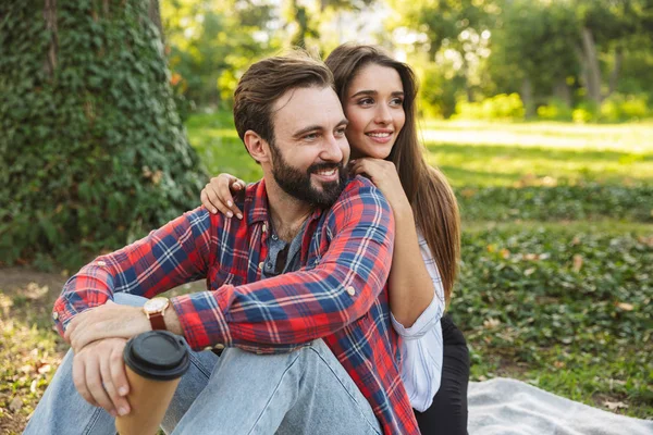 Imagen de pareja romántica hombre y mujer abrazando y bebiendo café para llevar mientras descansan en el parque verde — Foto de Stock