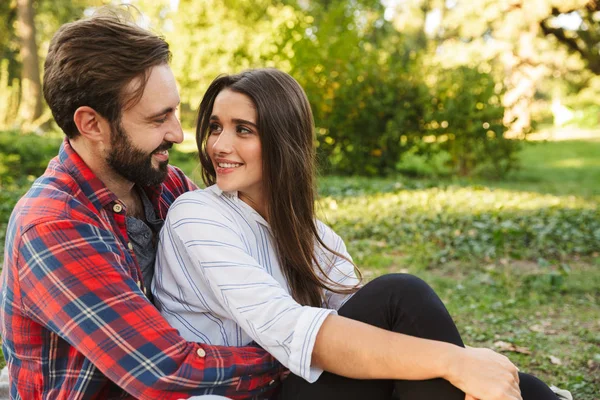 Bild eines optimistischen Paares, das sich im grünen Park umarmt und ansieht — Stockfoto