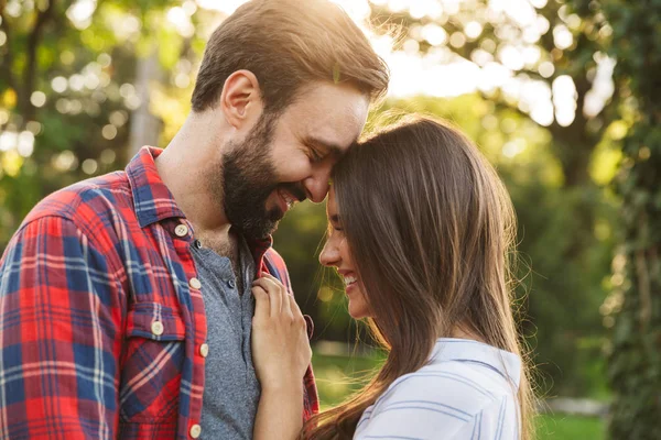 Imagine a unui cuplu tânăr bărbat și femeie îmbrățișându-se și zâmbind în timp ce mergeau în parc verde — Fotografie, imagine de stoc