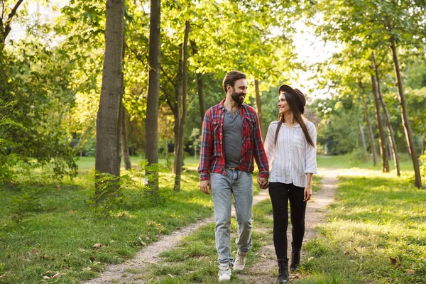 Yeşil bir doğa parkı ormanda açık havada yürüyen gülümseyen pozitif genç sevgi dolu çift. — Stok fotoğraf