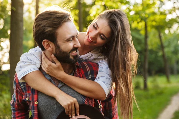 Image of caucasian man giving piggy back ride to pretty woman in green park — Stock Photo, Image