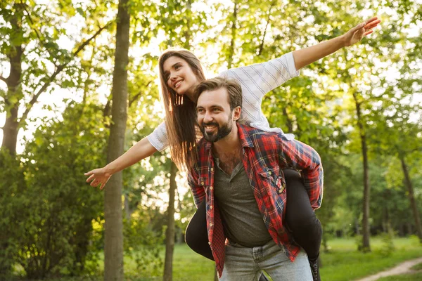 Imagen de hombre alegre dando paseo a cuestas a la mujer divertida en el parque verde —  Fotos de Stock