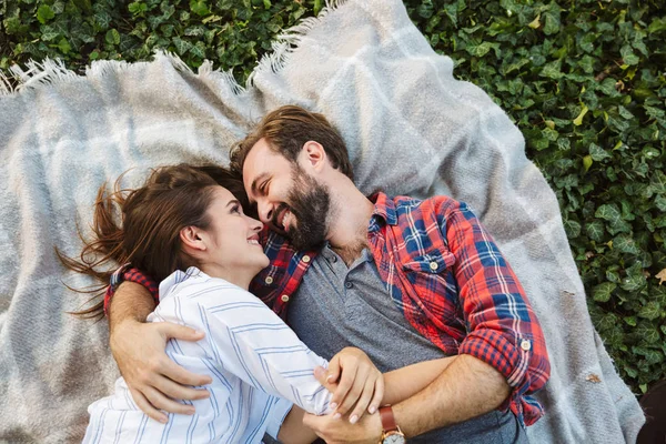 Yeşil parkta yatarken birbirlerine sarılan ve bakan genç çift erkek ve kadın görüntüsü — Stok fotoğraf