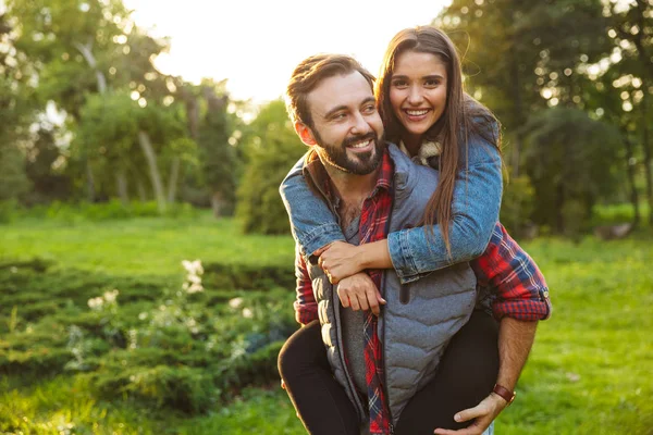 Bild eines lächelnden Mannes, der einer netten Frau Huckepack im grünen Park gibt — Stockfoto