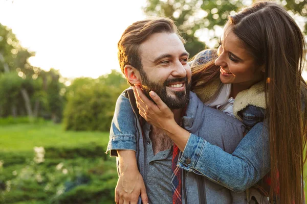 Image of smiling man giving piggyback ride to his girlfriend in green park — Stock Photo, Image