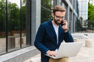 Cep telefonu yla konuşan ve dizüstü bilgisayar kullanan gözlük takan memnun işadamıportresi