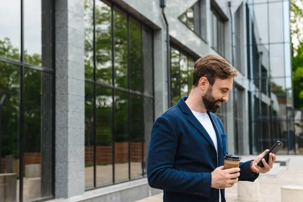 Портрет чоловічого бізнесмена в куртці, що тримає мобільний телефон, стоячи на відкритому повітрі — стокове фото