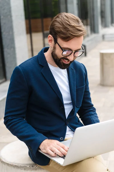 Porträt eines optimistischen Geschäftsmannes mit Brille und Blick auf Laptop — Stockfoto