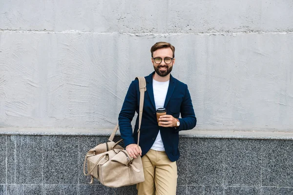 Портрет уверенного бизнесмена в очках, пьющего кофе из бумажной чашки и несущего сумку — стоковое фото