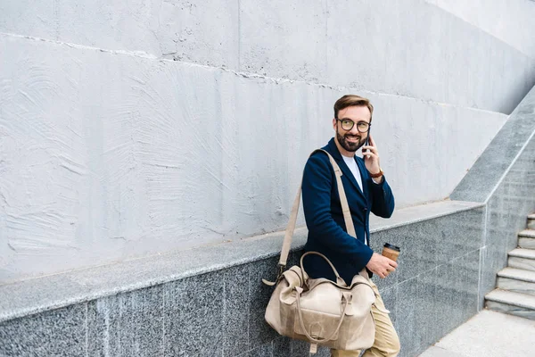Портрет білоруського бізнесмена в окулярах, що розмовляють на мобільному телефоні і тримають паперовий стаканчик і сумку — стокове фото