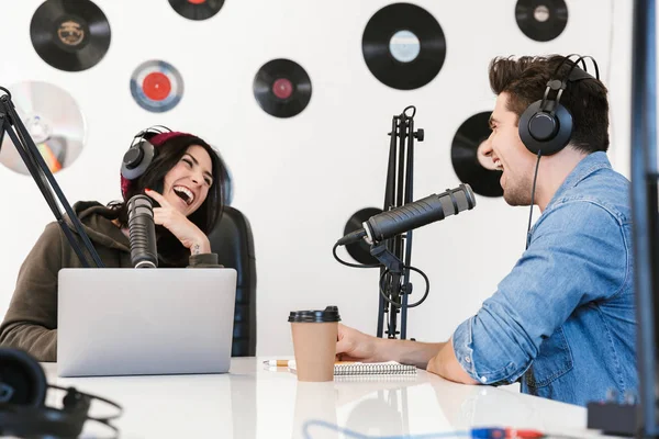 Hombre joven anfitrión de radio con la mujer colega en el espacio de trabajo con micrófono y equipo de sonido hablando entre sí . —  Fotos de Stock