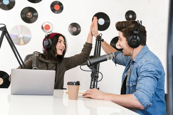 Hombre joven anfitrión de radio con la mujer colega en el espacio de trabajo con micrófono y equipo de sonido hablando entre sí . —  Fotos de Stock