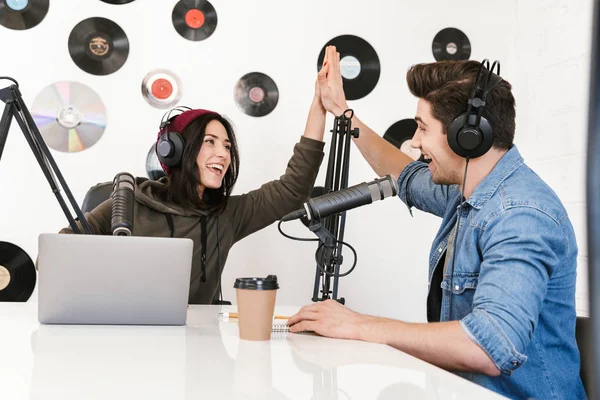 Hombre joven anfitrión de radio con la mujer colega en el espacio de trabajo con micrófono y equipo de sonido hablando entre sí . —  Fotos de Stock