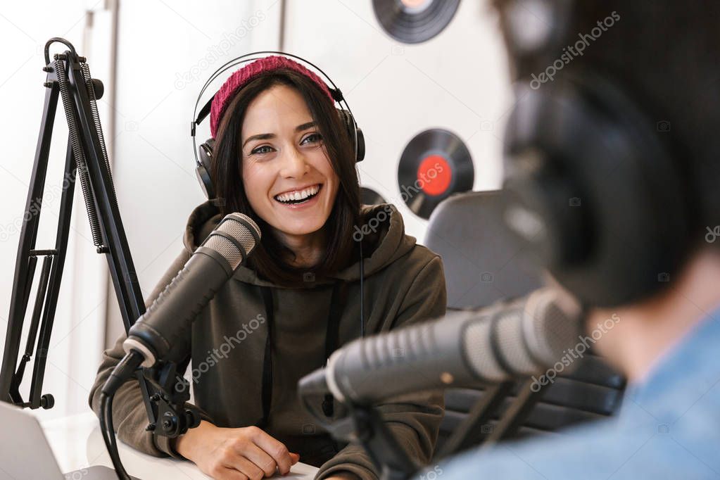 Young man radio host with colleague woman at the workspace with microphone and sound equipment talking with each other.