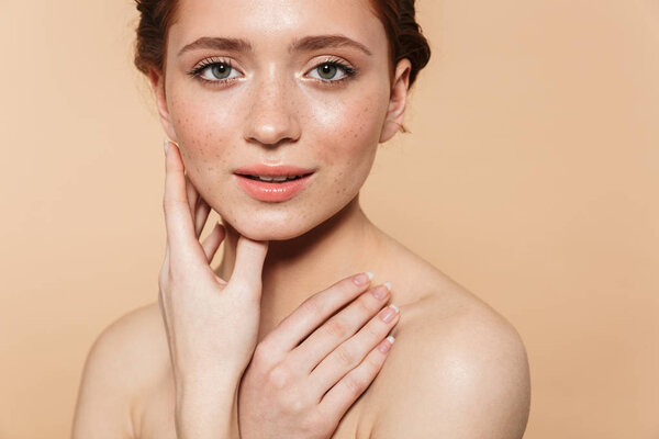 Young redhead woman posing isolated over beige wall background.