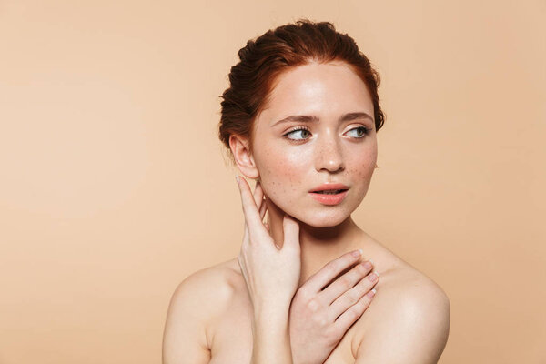 Young redhead woman posing isolated over beige wall background.