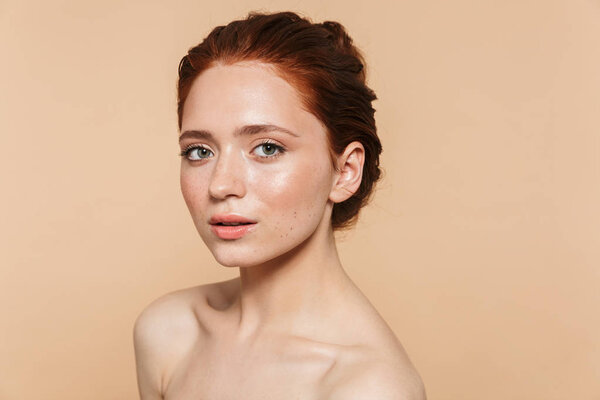 Young redhead woman posing isolated over beige wall background.