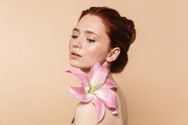 Pretty genç kızıl saçlı kadın bej duvar arka plan pembe çiçek üzerinde izole poz.