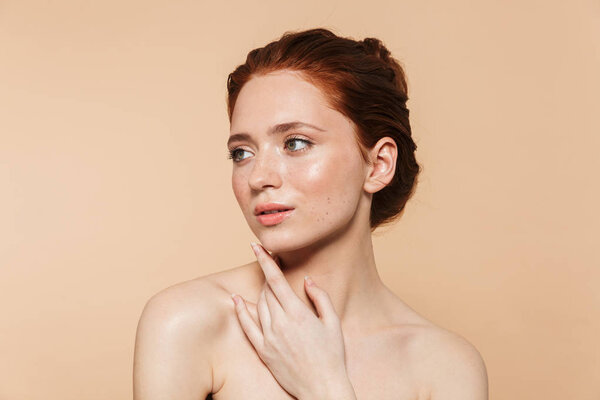Young redhead woman posing isolated over beige wall background.