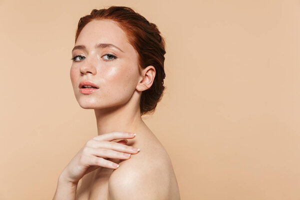 Young redhead woman posing isolated over beige wall background.