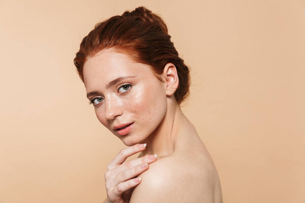 Young redhead woman posing isolated over beige wall background.