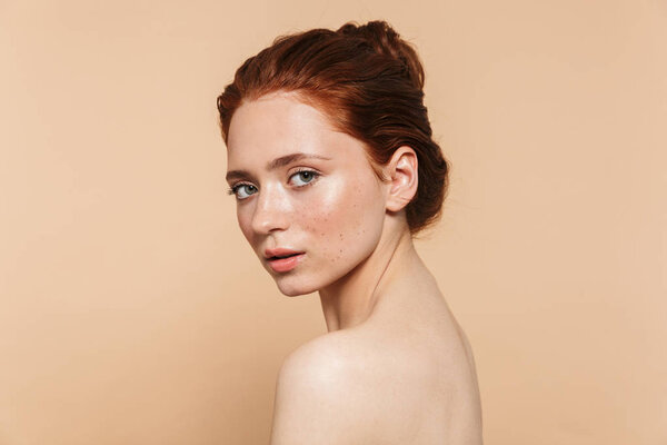 Young redhead woman posing isolated over beige wall background.