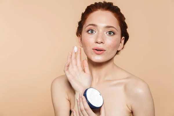 Increíble joven pelirroja posando aislada sobre fondo de pared beige cuidar su piel con crema . —  Fotos de Stock