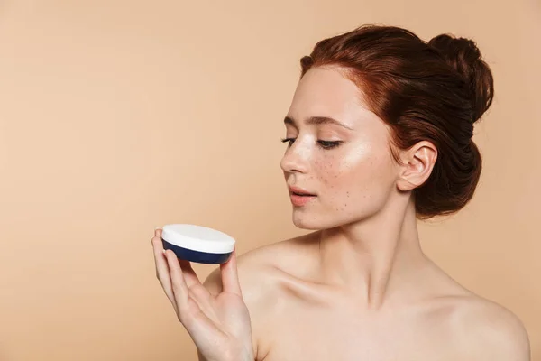 Increíble joven pelirroja posando aislada sobre fondo de pared beige cuidar su piel con crema . —  Fotos de Stock