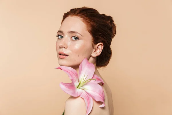 Mujer pelirroja bastante joven posando aislada sobre fondo de pared beige flor rosa . — Foto de Stock