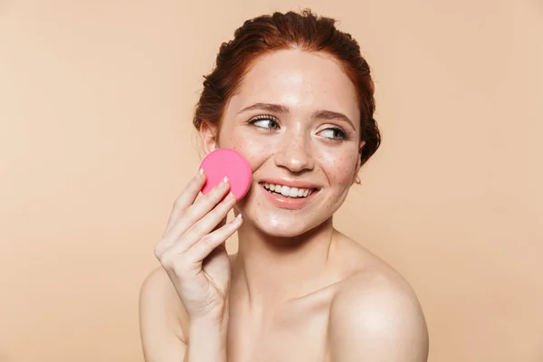 Jonge roodharige vrouw poseren geïsoleerd over beige muur achtergrond Holding make-up spons — Stockfoto