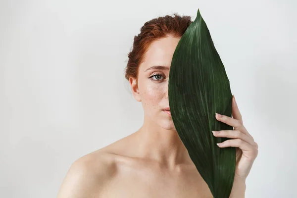 Joven pelirroja posando aislada sobre fondo blanco de pared con hojas de flores verdes . — Foto de Stock