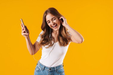 Cep telefonu ve kulaklıkla müzik dinlerken temel t-shirt şarkı giyen neşeli beyaz kadın görüntü