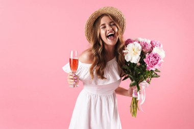 Çiçek ve şampanya bardağı tutarken gülerek hasır şapka giyen sarışın neşeli kadın görüntü