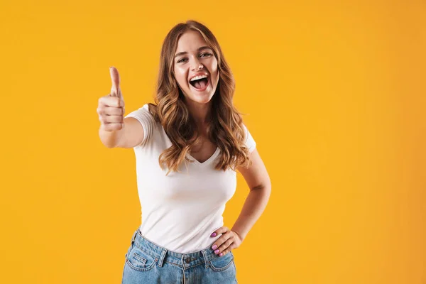 Felice emotivo sorridente ragazza in casual t-shirt bianca posa isolata su sfondo muro giallo mostrando pollici in su . — Foto Stock