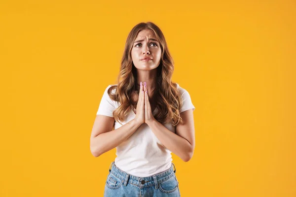 Menina esperançosa em casual t-shirt branca posando isolado sobre fundo de parede amarelo mostrando por favor rezar gesto . — Fotografia de Stock