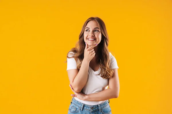 Vrolijk gelukkig meisje in Casual wit t-shirt poseren geïsoleerd over gele muur achtergrond kijken opzij. — Stockfoto