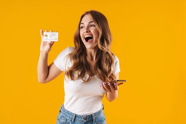Фото радостной молодой женщины, радующейся, держа в руках кредитную карту и смартфон — стоковое фото