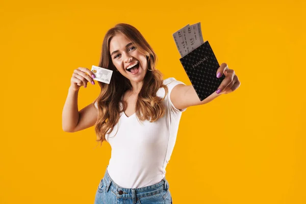 Фото щасливої молодої жінки, яка радіє, тримаючи кредитну картку і паспорт з проїзними квитками — стокове фото