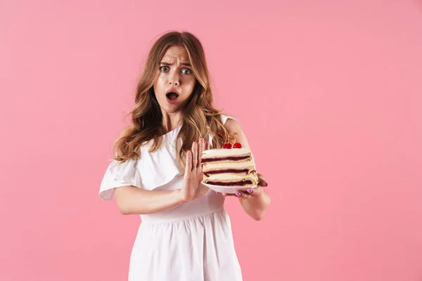 Immagine di donna confusa scioccata che indossa un vestito bianco facendo gesto di stop e tenendo in mano un pezzo di torta — Foto Stock