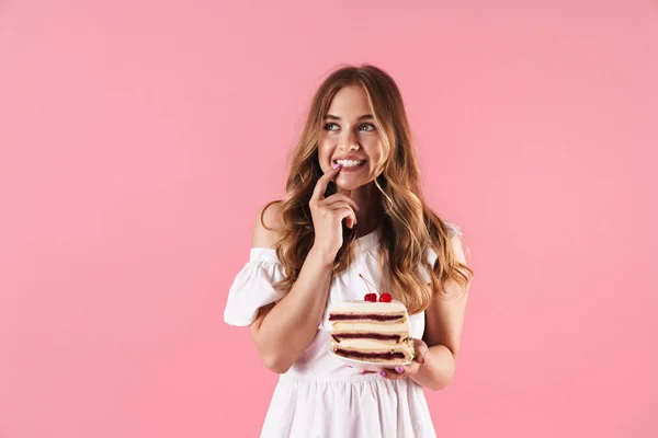 Bild av lyckligt tänkande kvinna klädd i vit klänning tittar uppåt med fingret på hennes tandens och håller Piece of Cake — Stockfoto