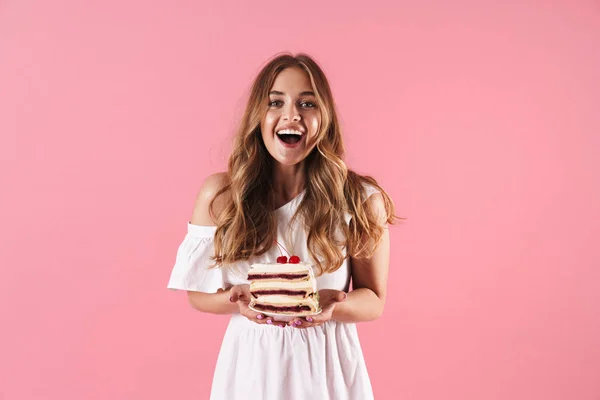 Imagen de la feliz mujer sorprendida vistiendo vestido blanco sonriendo a la cámara y sosteniendo un pedazo de pastel — Foto de Stock