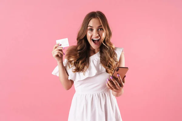 Smiling cheerful young pretty woman posing isolated over pink wall background using mobile phone holding credit card. — Stock Photo, Image