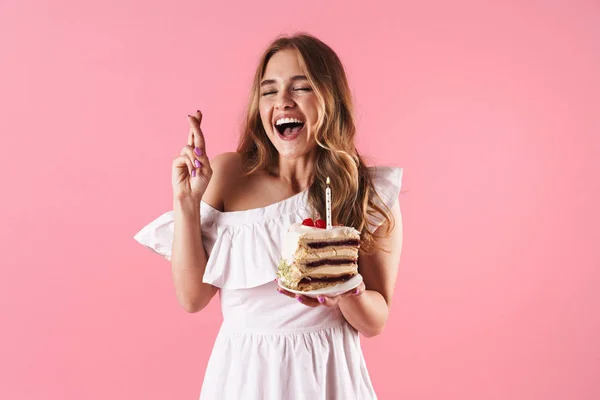 Imagen de una atractiva mujer riendo con vestido blanco sosteniendo los dedos cruzados y un pedazo de pastel con cand — Foto de Stock