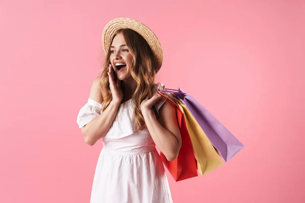 Imagen de una hermosa mujer asombrada con sombrero de paja preguntándose y sosteniendo bolsas de compras — Foto de Stock